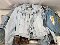 Pile of denim jackets and jeans showing different washes and a partially visible leopard print item underneath.