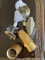 Photo showing all items including the metal wall sconce base, frosted glass shade, two light fixtures, and six gold paper shades arranged on table.