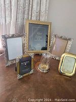 Group view of five picture frames and one dome clock on wooden table, showing varying frame sizes and designs