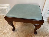 Angled side view of square footstool showing Queen Anne style curved legs with pad feet and teal leather upholstery on top.