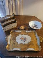 Lot of four items on table including Florentine tray, porcelain bowl, papier-mâché plaque, and wood magazine holder