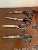 Four sewing shears laid flat on a wooden surface showing overall condition, blade styles, and handle shapes.