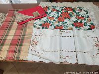 Overview of holiday linens including a plaid runner, floral tablecloth with lace border, and embroidered centerpiece mat