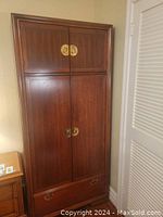 Front view of the vintage Kroehler rosewood veneer armoire showing upper and lower cupboard doors with brass hardware and bottom drawer