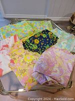 Seven fabric remnants arranged on glass table showing colorful retro and floral prints in various colors and patterns.