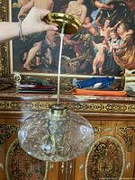 Photo showing the full pendant light held upright. Visible glass shade with bubble texture, brass canopy, and white cable.