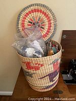 Full view of tall woven raffia basket with colorful design holding knitting supplies inside, showing overall size and pattern details