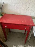 Full view of the desk showing cherry red painted wood with distressed worn finish, single drawer closed, square legs.