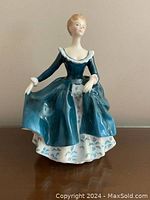 Front view of Royal Doulton Janine figurine in blue dress with white underskirt, showing the pose and detailed face and hair