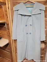 Front view of baby blue double-breasted wool coat with wide collar, decorative 1940s-era buttons, and stitched patch pockets.