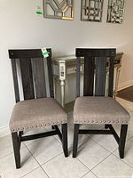 Pair of dark wood frame chairs with beige upholstered seats, nailhead trim detailing, and vertical slat backs.