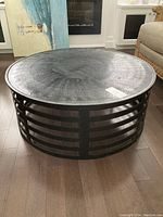 Front angle view of round metal coffee table showing textured top and slatted base.