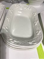 Photo of stacked white ceramic dishes with embossed decorative rims showing the details of the border pattern and shape of dishes.