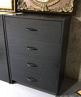 Black laminated dresser with four drawers, front view showing design and handles.