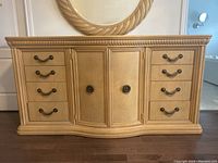 Front view of wood veneer dresser showing 7 drawers and central cabinet with two doors, light wood finish, decorative molding and metal handles.