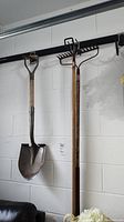 View of shovel and two rakes hanging on wall, showing handles and metal parts