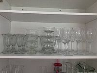 Shelf with 3 groups of clear glassware: 5 sherbet glasses on left, 5 dessert dishes stacked center, 5 wine glasses on right.