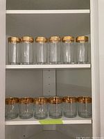 Two shelves of glasses. Top shelf has six tall clear glasses with gold rims. Bottom shelf has six shorter glasses with gold rims.