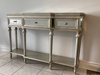 Front view showing three drawers with mirrored fronts, matching mirrored top, silver metallic finish, and turned front legs.