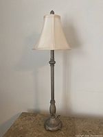 Full view of the tall lamp with beige fabric shade on a marble surface against a wall.