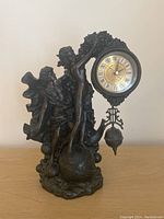 Front view showing two classical figures holding the ornate clock face and pendulum.