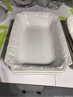 Photo of three stacked white rectangular ceramic serving dishes showing ornate raised floral decoration and handles. Taken to show design and condition.