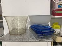 View of lot showing large clear textured glass bowl, large white plastic mixing bowl, and stack of blue-lid Pyrex glass baking dishes, plus rectangular Pyrex loaf pan on bottom right.