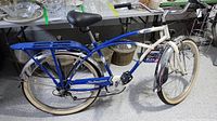 Full side view of the blue and white 5-Star Cruisers Schwinn bike with cream tires, rear cargo rack, and black saddle.
