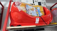 Side view of red plastic baby sled with packaging inside, placed on wooden surface