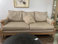 Front view of beige upholstered sofa with three back cushions, two seat cushions, and one decorative cushion. Carved wooden frame visible on arms and base.