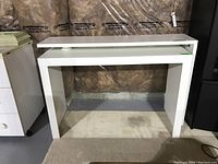 Full view of the two white laminate tables showing size and positioning, with one table featuring a narrower upper surface that swivels out.