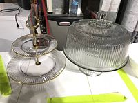 Glass two-tiered plate stand with gold accents alongside ribbed glass cake stand with dome lid