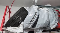 Four Michelin tires with rims stacked side by side wrapped partially in plastic bags showing brand name.