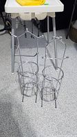 Two silver-tone metal toilet paper holders standing on floor next to white table with grey legs.