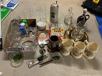 Overview photo showing all items in the lot including glasses, steins, bar tools, coasters, and metal beer sign arranged on table.