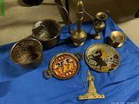 Photo showing all brass and ceramic items on a blue cloth including planters, decorative plates, candle holder, key rack, and small vase.