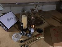 Overview of candle accessories including a large glass hurricane candle holder with candle, metal candle tray, glass holders, and metal candlesticks.