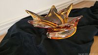 Chalet Glass abstract bowl with star-like points and translucent orange-amber glass color on black cloth background