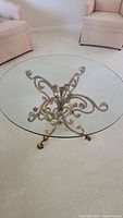 Full view of round glass top coffee table with metal scrolled antiqued bronze base and curved feet.