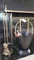 Full view of fireplace tool set on metal stand with black bucket nearby