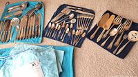 Overall view of flatware laid out on blue storage rolls and light blue Birks bag, showing knives, spoons, forks and serving utensils