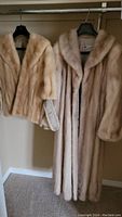 Two light beige fur coats hanging on a rack: a short jacket and a long coat.