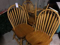 Four wooden hoop-back chairs in honey finish grouped in basement setting, front view showing seat shapes and spindle backs