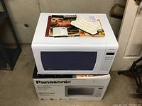 Panasonic microwave oven on its box with cookbooks and hot dog dish on top, showing overall lot contents