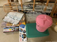 Photo of various organizing helpers including white metal wire racks, multiple types of hangers, two hanging divided canvas shoe holders, a pink plastic bucket and a green lid tote, packaged furniture lifters and sliders, and Amazing Hanger set.