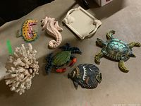 Overview photo showing painted wooden marine animal plaques, natural coral, ceramic platter with shell handles, and bag.