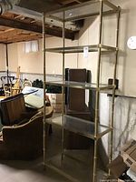 Full view of brass-colored metal shelving unit with five glass shelves against basement wall