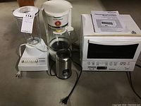 Four small kitchen appliances displayed: Hamilton Beach blender, drip coffee maker, Panasonic toaster oven with manual, and Salton coffee grinder.