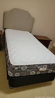 Full view of the twin bed including headboard, mattress, and boxspring showing the floral pattern on boxspring and white pillowtop mattress.