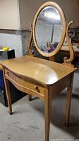 Full view of the vanity table showing the birdseye maple top, dovetail drawer, and attached oval harp mirror.
